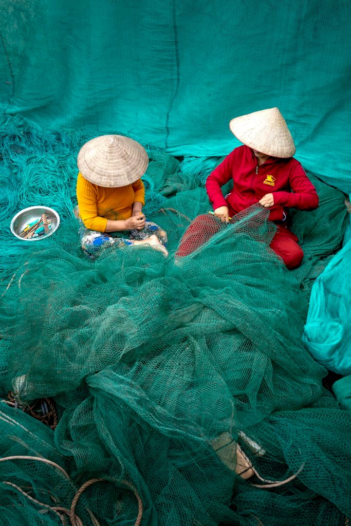 Fishermen in Vietnam repair fishing nets, showcasing traditional attire and vibrant colors.